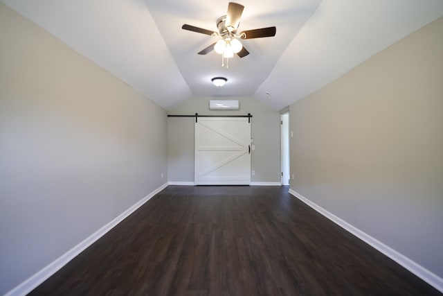 spare room with a barn door, dark hardwood / wood-style floors, vaulted ceiling, and ceiling fan