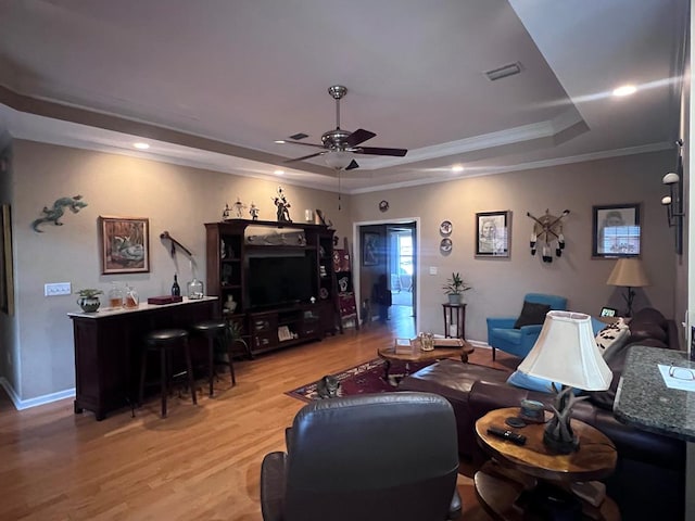 living room with ceiling fan, visible vents, a tray ceiling, light wood finished floors, and crown molding