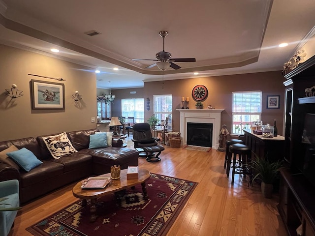 living room with visible vents, a tray ceiling, a healthy amount of sunlight, light wood-style floors, and a fireplace