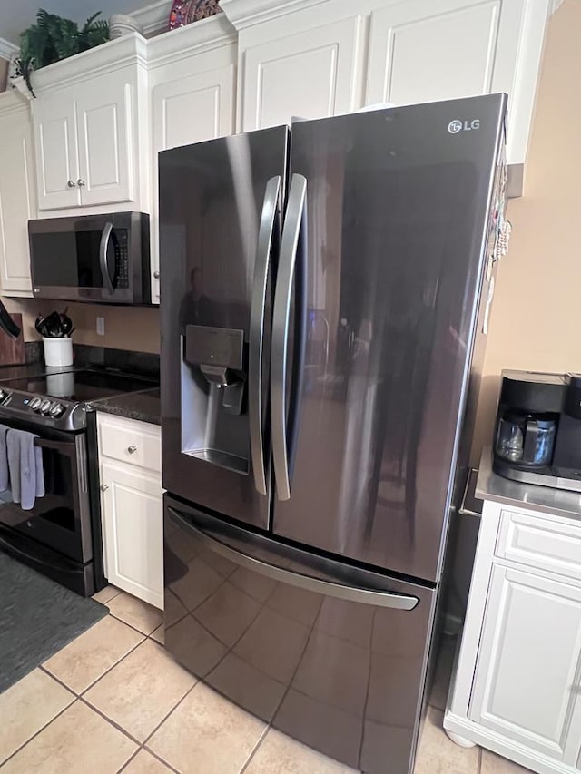 kitchen featuring light tile patterned floors, dark countertops, electric range, white cabinets, and stainless steel fridge