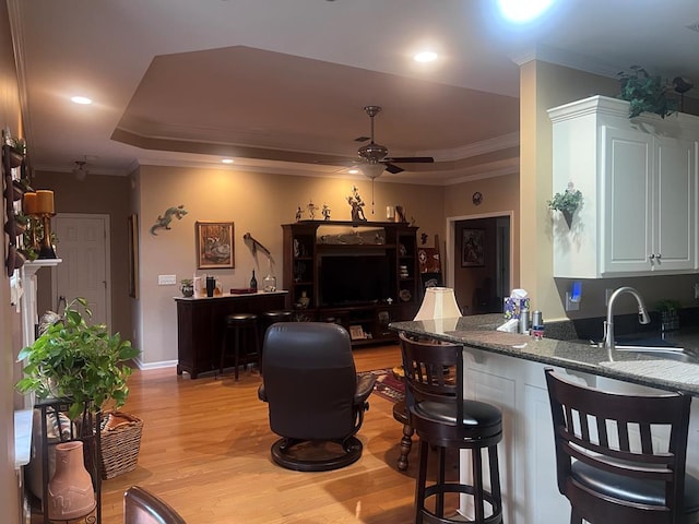 kitchen featuring a tray ceiling, ornamental molding, a ceiling fan, a sink, and light wood-type flooring