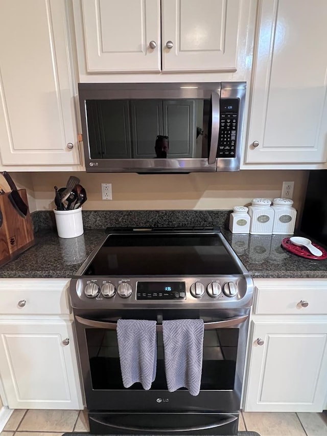 kitchen featuring dark stone counters, appliances with stainless steel finishes, light tile patterned flooring, and white cabinetry