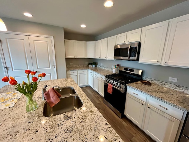 kitchen with sink, white cabinetry, appliances with stainless steel finishes, dark hardwood / wood-style flooring, and light stone countertops