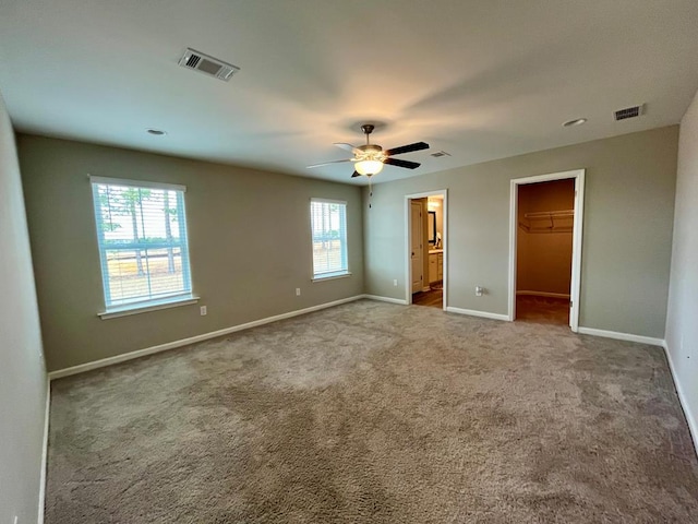 unfurnished bedroom with ensuite bathroom, a spacious closet, carpet floors, a closet, and ceiling fan