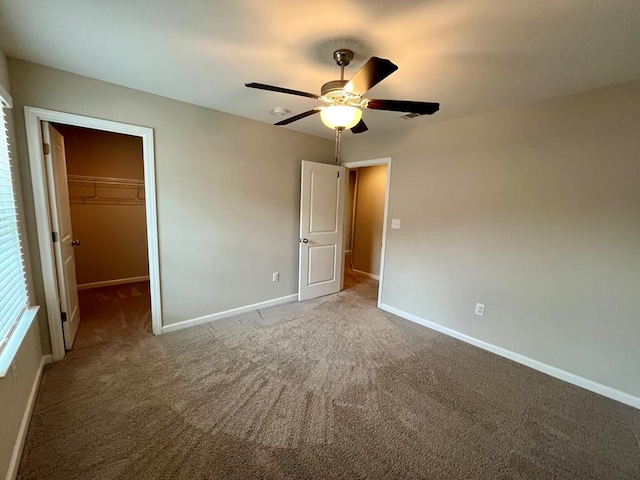 unfurnished bedroom featuring a walk in closet, carpet floors, a closet, and ceiling fan