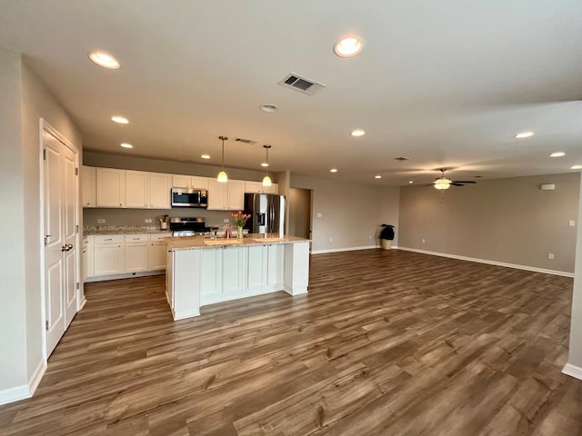 kitchen featuring pendant lighting, stainless steel appliances, dark hardwood / wood-style floors, white cabinets, and a center island with sink