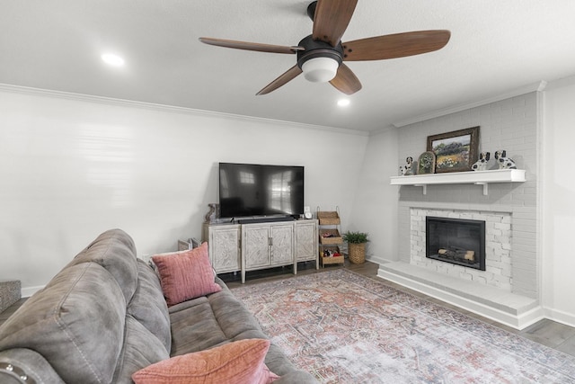 living room with crown molding, a ceiling fan, a brick fireplace, and wood finished floors