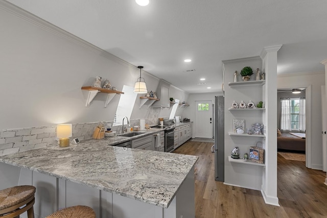 kitchen with open shelves, appliances with stainless steel finishes, light stone countertops, a sink, and a peninsula