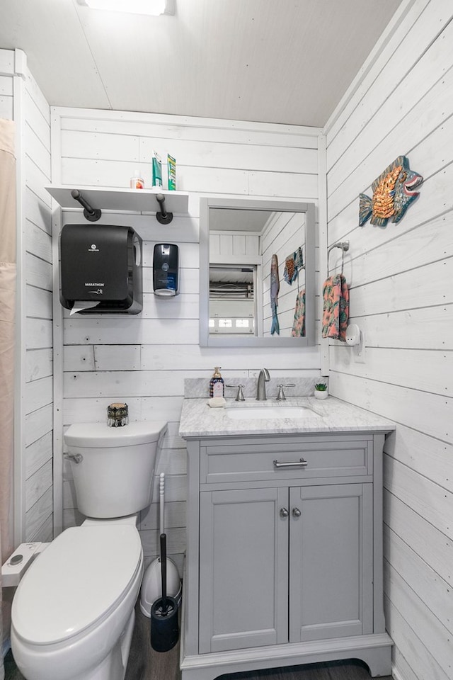 bathroom featuring vanity, wooden walls, and toilet