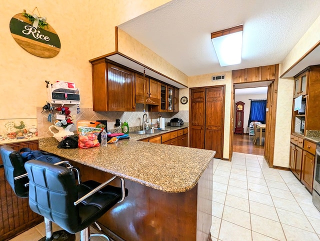 kitchen featuring kitchen peninsula, a kitchen bar, backsplash, sink, and light tile patterned flooring