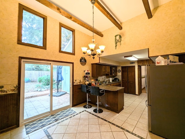 kitchen with stainless steel fridge, a breakfast bar, dark brown cabinetry, a notable chandelier, and beamed ceiling