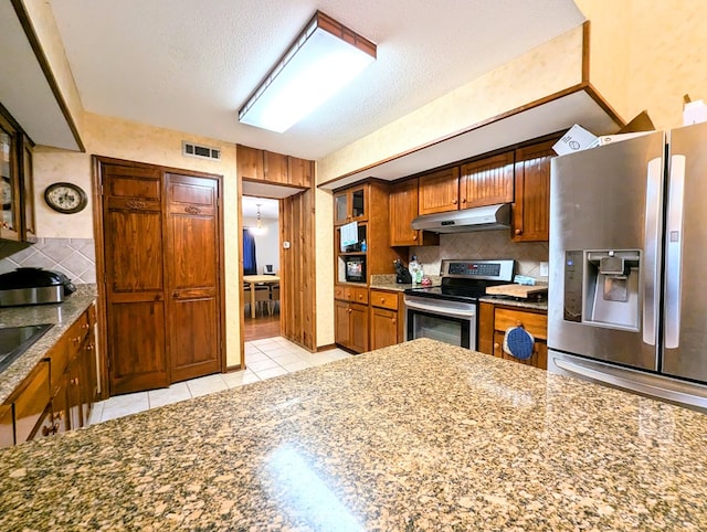 kitchen featuring appliances with stainless steel finishes, a textured ceiling, tasteful backsplash, and light tile patterned floors