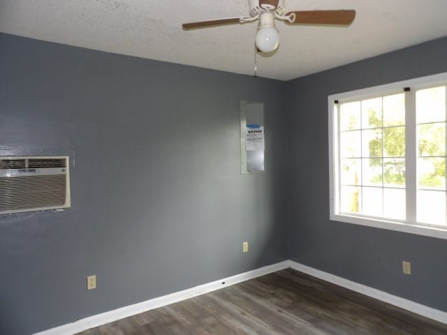 empty room featuring ceiling fan, dark wood-type flooring, and a wall mounted AC