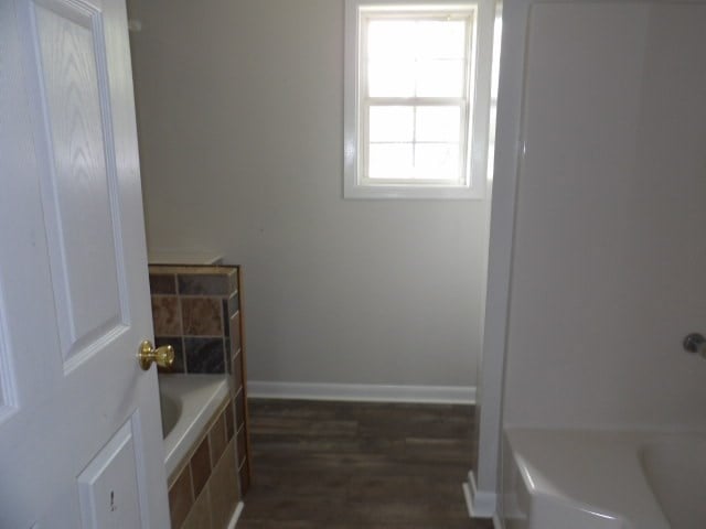 bathroom with tiled tub and wood-type flooring