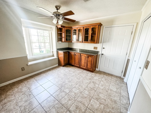 kitchen featuring ceiling fan, glass insert cabinets, brown cabinetry, a textured ceiling, and dark countertops