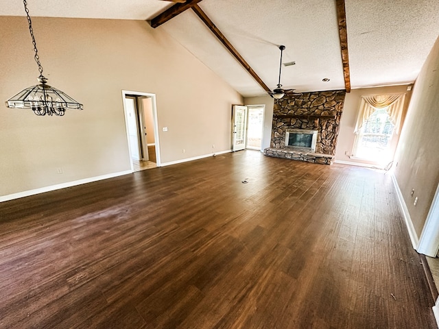 unfurnished living room with ceiling fan with notable chandelier, beamed ceiling, a fireplace, dark wood finished floors, and baseboards