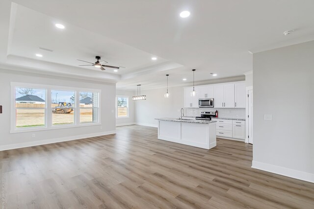 unfurnished living room featuring a tray ceiling, ceiling fan, sink, and light wood-type flooring