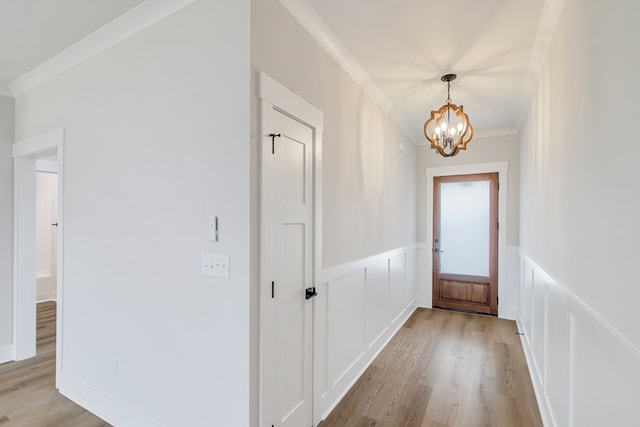 doorway to outside featuring ornamental molding, an inviting chandelier, and light hardwood / wood-style flooring