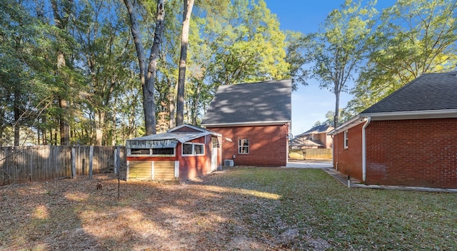 rear view of house with a lawn, brick siding, fence, an outdoor structure, and a shingled roof