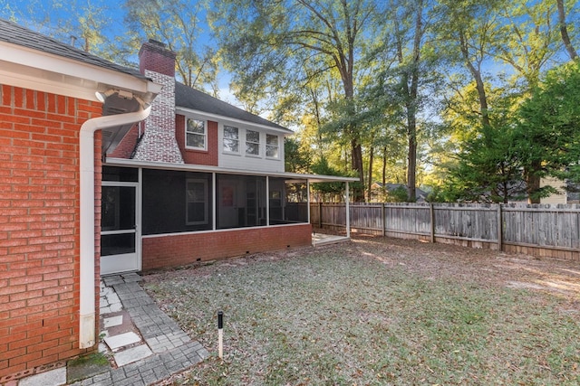 rear view of house with fence, roof with shingles, a chimney, a sunroom, and brick siding