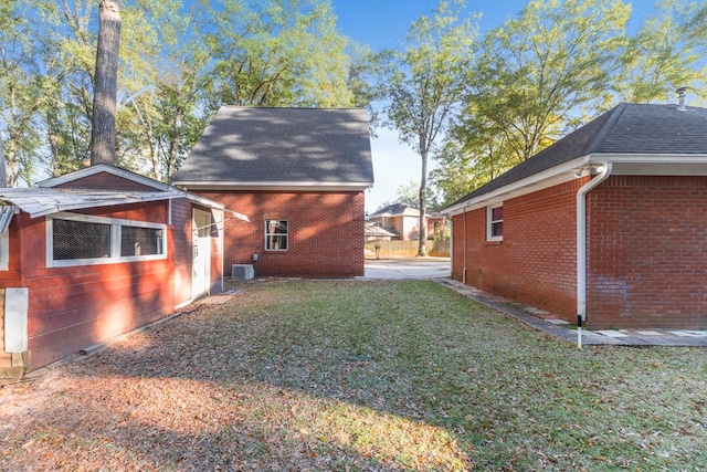 view of side of property with an outdoor structure, a shingled roof, a yard, and brick siding