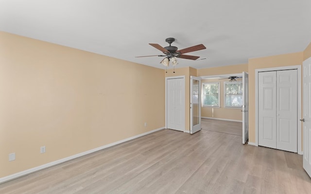 unfurnished bedroom featuring a ceiling fan, baseboards, multiple closets, and light wood-style flooring