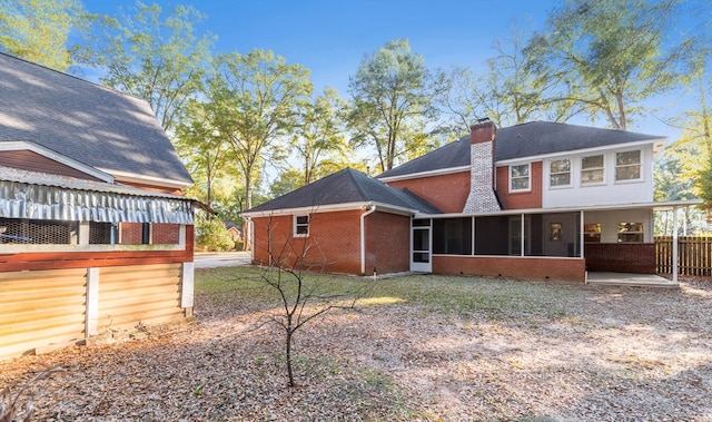 rear view of house with a sunroom, a shingled roof, brick siding, and a chimney