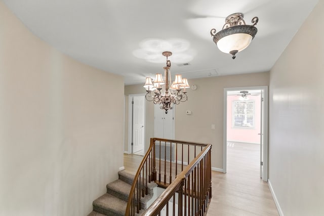 hallway with visible vents, light wood-type flooring, baseboards, an upstairs landing, and an inviting chandelier