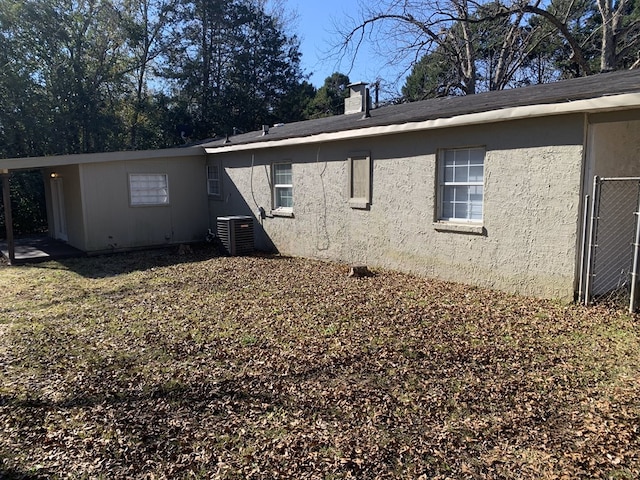 view of side of home with a chimney, cooling unit, and stucco siding