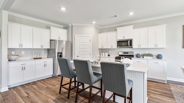 kitchen with appliances with stainless steel finishes, light hardwood / wood-style floors, white cabinetry, and a kitchen island with sink