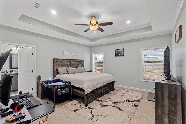 carpeted bedroom featuring a tray ceiling, ensuite bath, ceiling fan, and crown molding