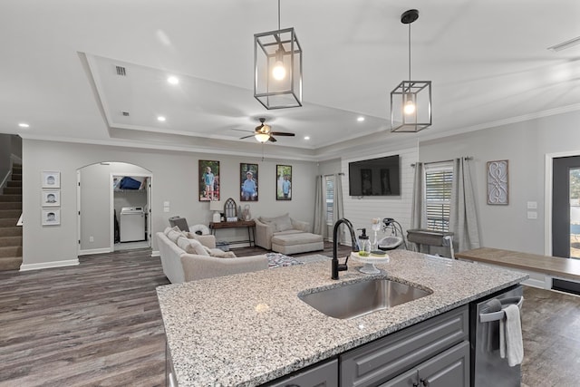 kitchen with a center island with sink, light stone countertops, sink, and hanging light fixtures