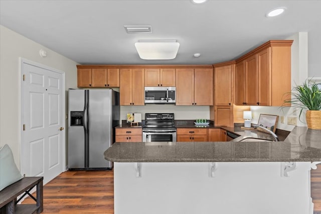 493 Shiloh Rd, Hartford, AL 36344 - kitchen with appliances with stainless steel finishes, a peninsula, dark wood-type flooring, a breakfast bar area, and dark stone countertops