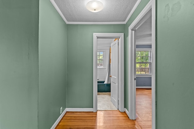 corridor with wood finished floors, a textured ceiling, crown molding, and baseboards