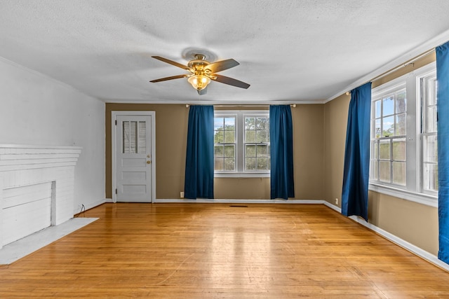 unfurnished room with light wood-style flooring, a ceiling fan, a textured ceiling, a fireplace, and crown molding