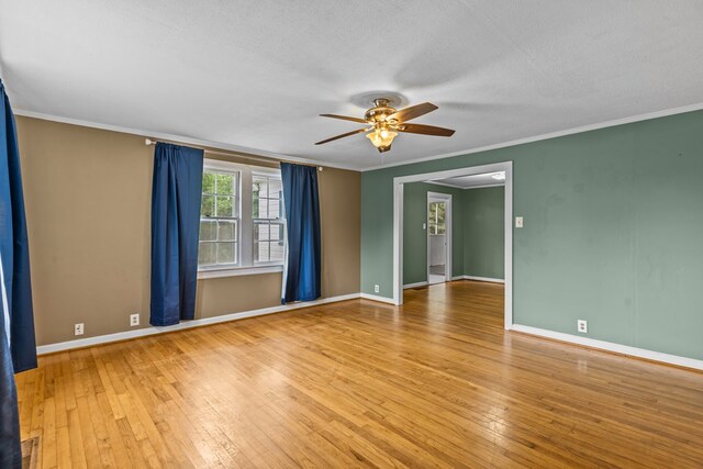 empty room with a ceiling fan, wood-type flooring, crown molding, and baseboards