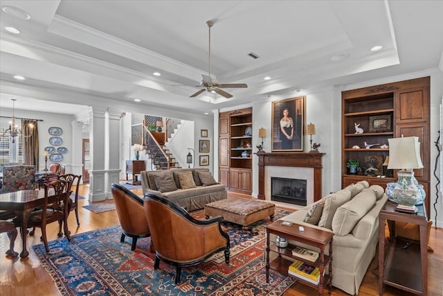 living room with built in features, a tray ceiling, a fireplace, and ornate columns