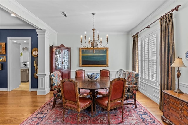 dining room with light wood-style floors, decorative columns, crown molding, and a notable chandelier