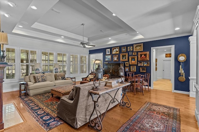 living room with ceiling fan, a tray ceiling, wood finished floors, and ornamental molding