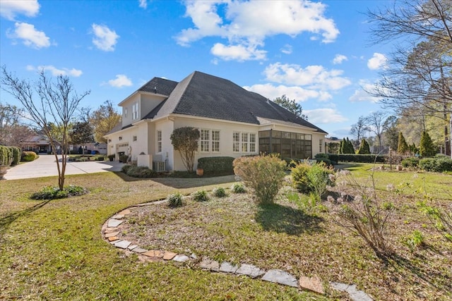 view of side of home with stucco siding, a lawn, central AC unit, a sunroom, and driveway