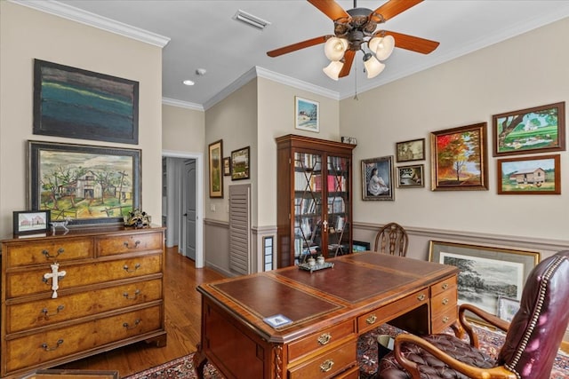 office space featuring dark wood-style flooring, visible vents, ornamental molding, a ceiling fan, and wainscoting