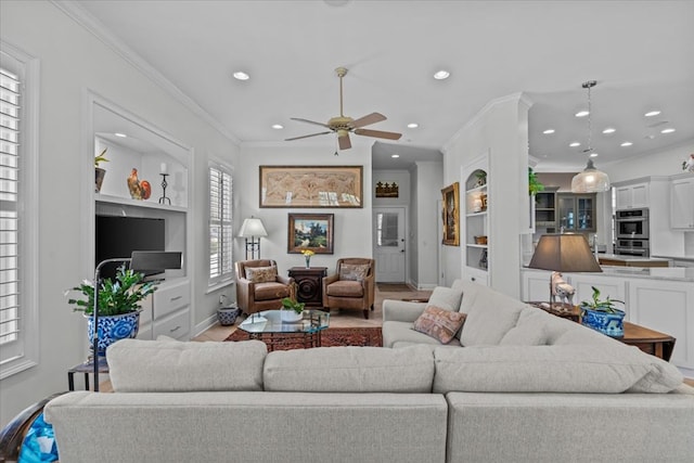 living area featuring built in shelves, recessed lighting, ornamental molding, ceiling fan, and baseboards