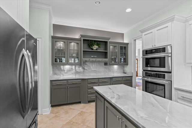 kitchen with light stone counters, stainless steel appliances, gray cabinets, decorative backsplash, and crown molding