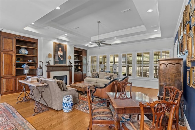 living room featuring light wood finished floors, a fireplace, a tray ceiling, and crown molding