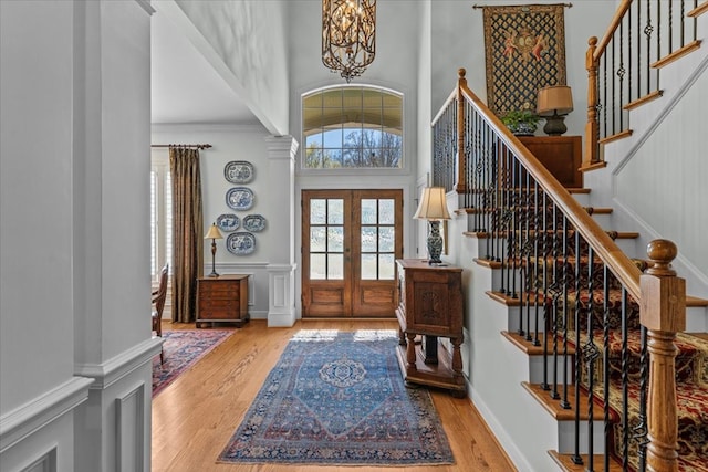 entrance foyer featuring french doors, wood finished floors, a towering ceiling, and a decorative wall