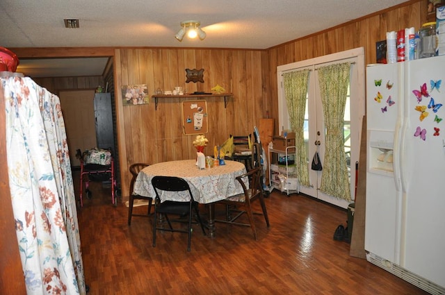 dining space featuring wood walls, french doors, dark wood-type flooring, and a textured ceiling