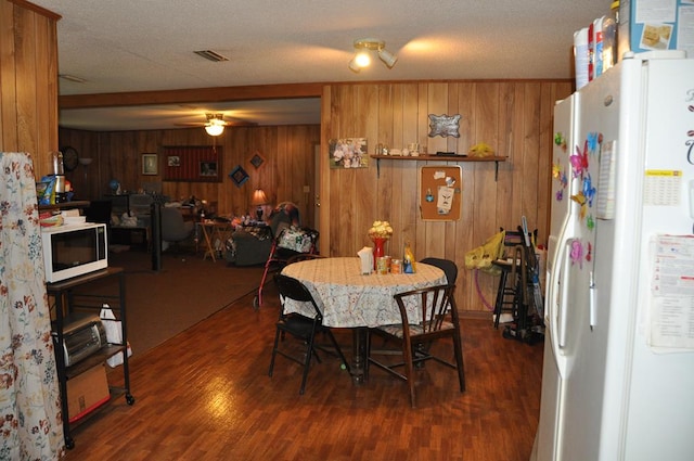 dining room with a textured ceiling, dark hardwood / wood-style floors, ceiling fan, and wood walls