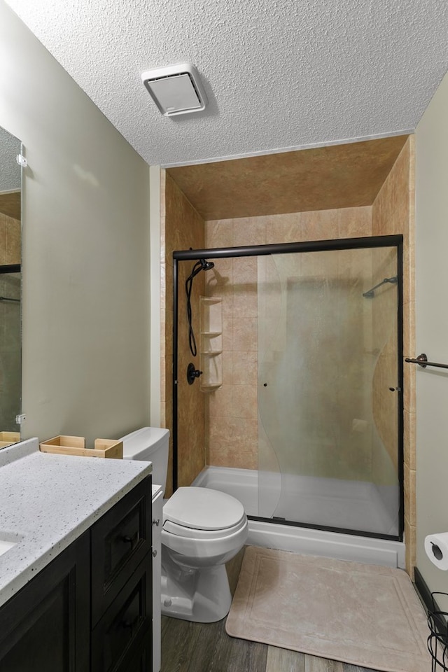 bathroom featuring toilet, vanity, a shower stall, wood finished floors, and a textured ceiling