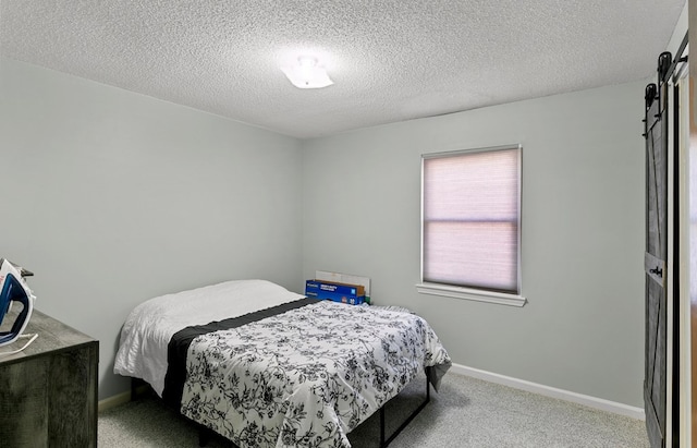 carpeted bedroom featuring a textured ceiling, baseboards, and a barn door