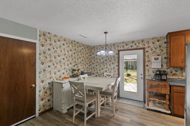 dining area with wood finished floors, a textured ceiling, an inviting chandelier, and wallpapered walls